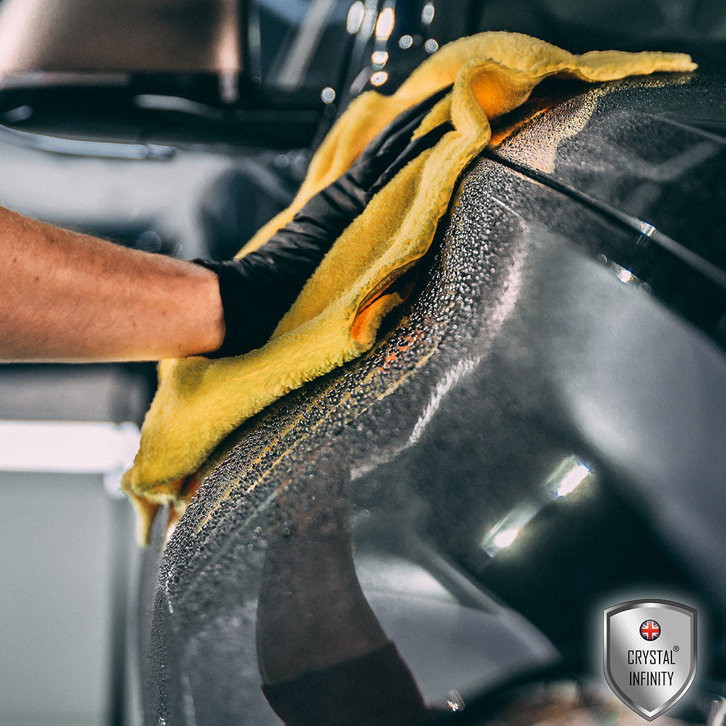 Person cleaning a car with a yellow microfibre close up